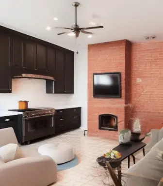 view of a living room kitchen combination, kitchen in back, painted brick walls in white, fireplace with art over the mantle, re
